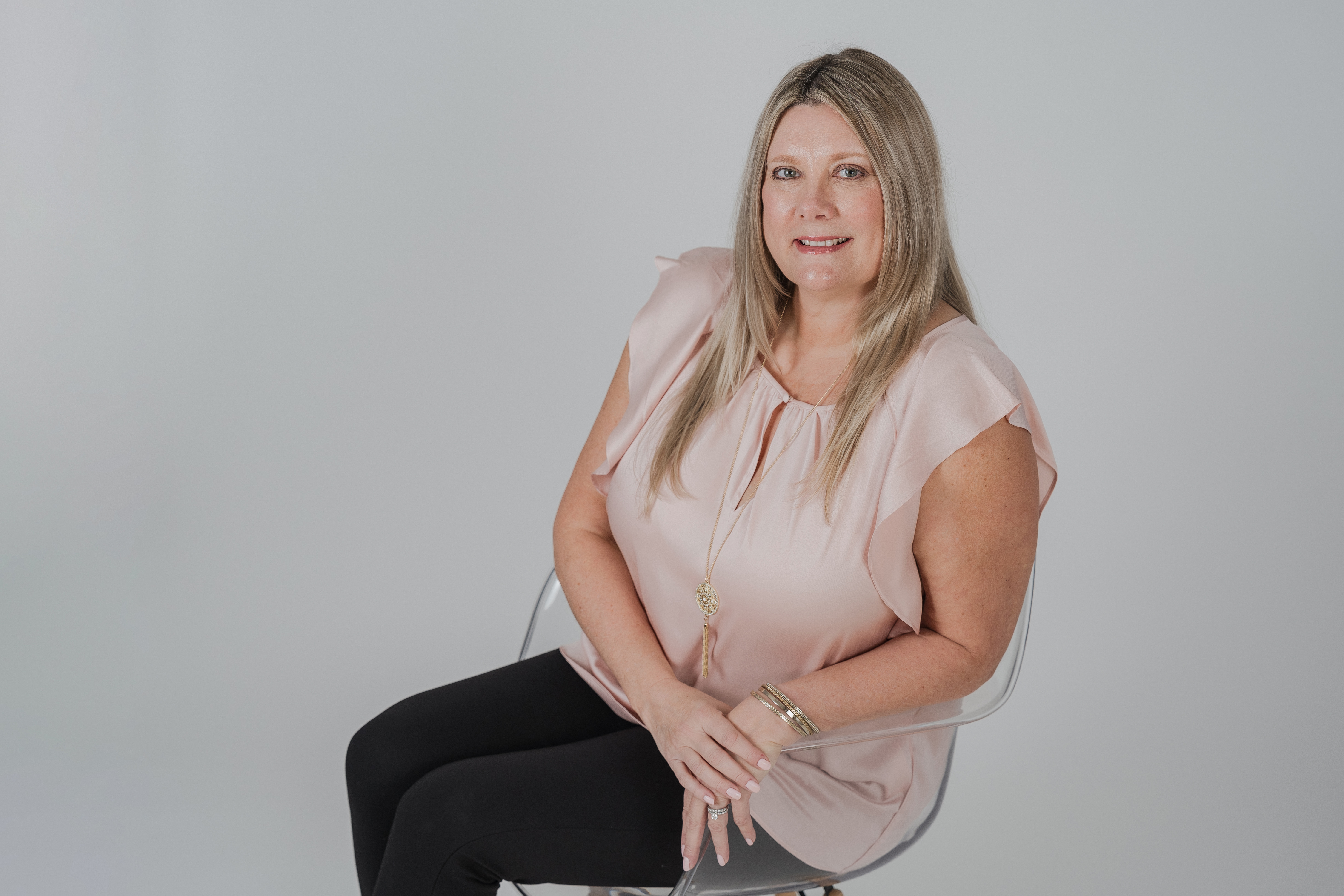 cathy saputo sitting in a chair leaning toward camera wearing pink shirt and black pants